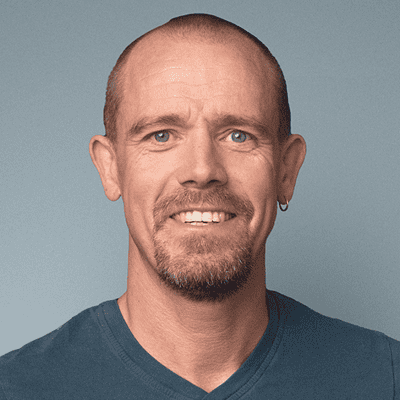 A person wearing a casual short‑sleeved shirt is shown from the shoulders upward in front of a solid-colored background.