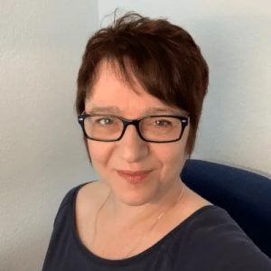 Portrait of a woman with short dark hair and black glasses smiling at the camera against a light background