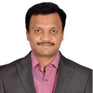 Professional head‑and‑shoulders portrait of a man wearing a dark suit jacket over a pink shirt, looking directly at the camera with a neutral expression against a plain white background.