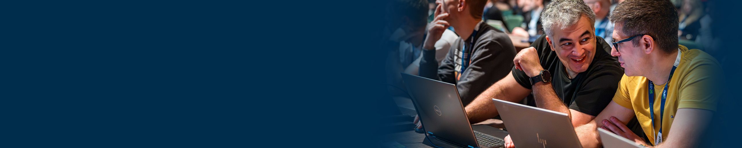 Two men sitting in a session room with laptops in front of them, smiling while sharing a conversation